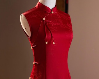 May include: A sleeveless red dress with a mandarin collar and pearl buttons. The dress has a traditional Chinese design and is made of a silky fabric.
