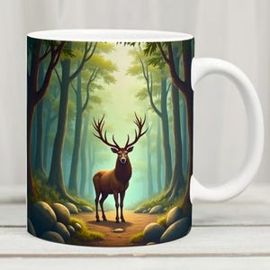 Könnte beinhalten: Weiße Keramiktasse mit einer detaillierten Illustration eines braunen Hirsches mit großem Geweih in einem Wald. Das Kunstwerk umfasst hohe Bäume, Felsen und einen Pfad und schafft eine ruhige Waldszene. Perfekt für Heißgetränke.