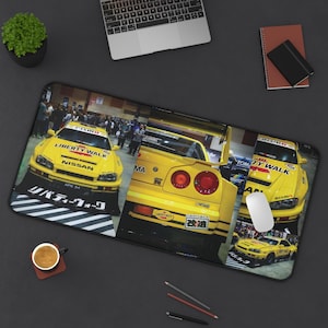 May include: A rectangular desk mat featuring a collage of yellow Nissan Skyline GT-R sports cars with Liberty Walk branding. The design includes front and rear views of the vehicles, Japanese text, and the words Liberty Walk and Nismo printed clearly.