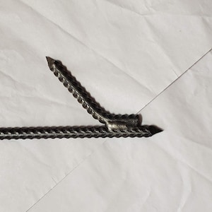 May include: A close-up of a metal rebar with a welded joint. The rebar is twisted and has a pointed end.