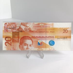 Op de afbeelding: Een Filipijnse bankbiljet van twintig peso, voornamelijk oranje en bruin, met het nummer "20" prominent weergegeven. De bankbiljet bevat portretten en tekst in het Engels en Tagalog, waaronder "Republika ng Pilipinas" en serienummers.