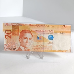 Op de afbeelding: Een Filipijnse bankbiljet van twintig peso, met een portret van een man in pak en vlinderdas. De biljet heeft de tekst "DALAWAMPUNG PISO" en "REPUBLIKA NG PILIPINAS". Het serienummer "WP472989" is zichtbaar. De biljet zit in een transparante plastic hoes.