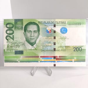 Może przedstawiać: Zielony i biały banknot 200 peso filipińskich. Banknot przedstawia portret mężczyzny, tekst "REPUBLIKA NG PILIPINAS" i nominał "200". Banknot jest prezentowany w przezroczystym plastikowym uchwycie.