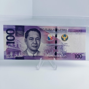 Puede incluir: Un billete de banco filipino de 100 pesos, de color morado y amarillo, con el retrato de un hombre con una camisa blanca y una corbata morada. El texto "REPUBLIKA NG PILIPINAS" y "SANDAANG PISO" está impreso en el billete. El número de serie "EK777777" está impreso en el lado derecho del billete.