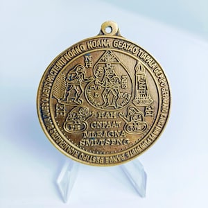 Könnte beinhalten: Ein runder, bronzefarbener Anhänger mit einem komplizierten Design, das ein zentrales Bild eines Mannes mit einer Krone und einem Wassertropfen zeigt. Der Anhänger ist mit den Worten "GEATAO TIAPALA GEPIPO GEPARATO CRISTUM PEPUM BISTE BANGE BESTIPO RICHARS", "HAH GNPAAN MLEAGNA SMLTSFNG" und "SHM HPN ΣΙΛΙ MILAM CVB TAL NH" beschriftet.
