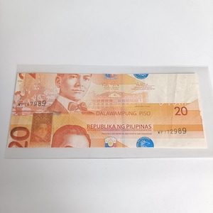 Op de afbeelding: Een Filipijnse bankbiljet van twintig peso, voornamelijk oranje en bruin, met een portret van een man in pak en vlinderdas. De biljet bevat tekst in het Engels en Tagalog, met het serienummer WP747989 zichtbaar.