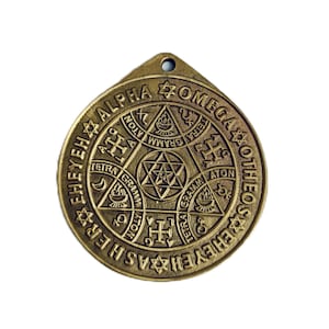 Pode incluir: Um pingente de metal dourado com um design circular que apresenta uma estrela de Davi, uma cruz e outros símbolos. O pingente é inscrito com as palavras "Alpha Omega Ehey Ehas Ehey Otheos".