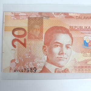 Op de afbeelding: Een Filipijnse bankbiljet van twintig peso, met een portret van een man en het woord "REPUBLIKA". De rekening is overwegend perzik en bruin van kleur, met het nummer "20" duidelijk zichtbaar. Het serienummer "WN447989" is afgedrukt.