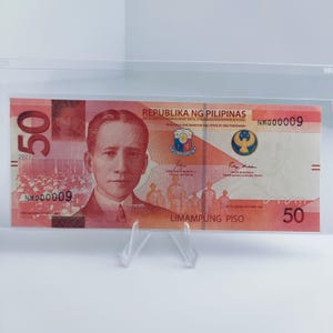 May include: A red and white Philippine 50 peso banknote with the text "REPUBLIKA NG PILIPINAS" and "LIMAMPUNG PISO" printed on it. The banknote features a portrait of a man and a seal with a bird.