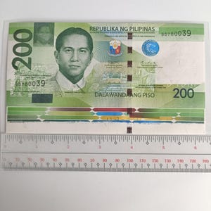 Könnte beinhalten: Ein philippinischer 200-Peso-Geldschein mit einem Porträt eines Mannes auf der Vorderseite. Die Banknote ist hauptsächlich grün mit Text in Englisch und Tagalog. Die Seriennummer BD780039 ist sichtbar. Ein Lineal ist darunter platziert.