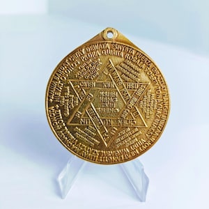 Puede incluir: Un colgante de metal dorado con un diseño circular que presenta una estrella de seis puntas con texto en varios idiomas. El texto incluye palabras como "DEWATA", "QUIRITA", "ROSALA", "SOERITY", "HSIEN", "HENG", "TSUI", "SHENG", "CHIEN", "KUN", "HSU", "KAN", "CHIEN", "KD", "NIW", "TLANGYA", "LLIVAY", "MACMASYN", "CASALXZATYZMASY", "NONOTA", "AMIIMBA", "TUNG", "JEN", "OROMACRAM", "METROLOMNOS", "MING", "PROVIDENCIA", "ENDI", "PROVIDERS", "YEN", "ESNYBTNFUERZA", "GRAZZTAY", "HANGTINITZAN", "PADRA", "ROSALA", "SOERITY", "TO", "NAYNAZ", "UTAGS".