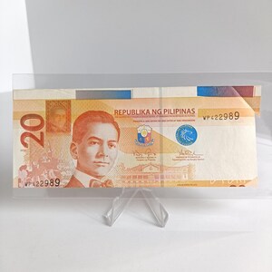 Könnte beinhalten: Eine philippinische 20-Peso-Banknote, die in einem transparenten Acrylhalter ausgestellt ist. Die Banknote zeigt ein Porträt eines Mannes und den Text "REPUBLIKA NG PILIPINAS". Die Banknote wird von einem transparenten Kunststoffständer gehalten.