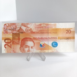 Op de afbeelding: Een Filipijnse bankbiljet van twintig peso, met portretten en tekst in het Engels en Tagalog. De bankbiljet is overwegend oranje en bruin, met het nummer 20 prominent weergegeven. De tekst bevat "Republika ng Pilipinas" en "Dalawampung Piso."