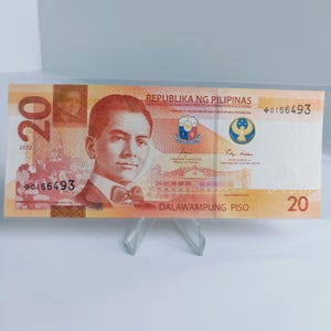 Könnte beinhalten: Ein zwanzig-Peso-Schein aus den Philippinen mit dem Porträt eines Mannes mit Fliege. Der Schein ist mit 2022 datiert und trägt den Text "REPUBLIKA NG PILIPINAS" und "DALAWAMPUNG PISO".
