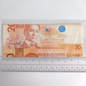Op de afbeelding: Een Filipijnse bankbiljet van twintig peso, met een portret van een man in pak en vlinderdas. De biljet heeft de tekst "DALAWAMPUNG PISO" en "REPUBLIKA NG PILIPINAS". Een liniaal is eronder geplaatst.