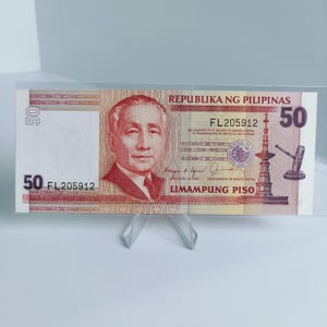 Puede incluir: Un billete de banco filipino de 50 pesos rojo y blanco con el texto "REPUBLIKA NG PILIPINAS" y "LIMAMPUNG PISO" impreso en él. El número de serie "FL205912" está impreso en el billete.