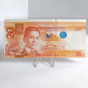 Könnte beinhalten: Eine philippinische 20-Peso-Banknote mit einem Porträt eines Mannes in Anzug und Fliege. Die Banknote ist überwiegend orange und braun, mit Text in Englisch und Tagalog. Das Jahr 2019 ist sichtbar.