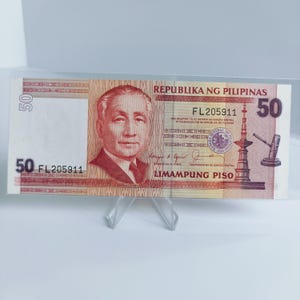 Puede incluir: Un billete de banco filipino de 50 pesos rojo y blanco con el texto "REPUBLIKA NG PILIPINAS" y "LIMAMPUNG PISO" impreso en él. El billete presenta un retrato de un hombre y una representación de un edificio con un cañón.