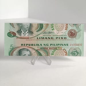 Könnte beinhalten: Eine philippinische Fünf-Peso-Banknote, überwiegend grün, mit Porträts historischer Persönlichkeiten und Text in Tagalog und Englisch. Enthält den Text "REPUBLIKA NG PILIPINAS" und "LIMANG PISO". Die Banknote wird auf einem transparenten Acrylständer präsentiert.