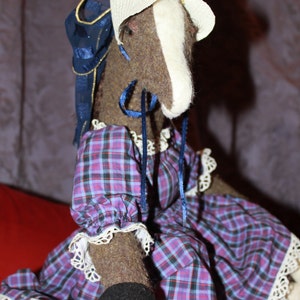 May include: A plush horse toy wearing a white hat with a blue ribbon and a purple and blue plaid dress with white lace trim.