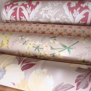 May include: Four rolls of wallpaper with floral and botanical designs. The top roll features a red and white floral pattern. The second roll has a small, repeating floral pattern in red and blue. The third roll has a bird and floral design. The bottom roll has large yellow flowers.