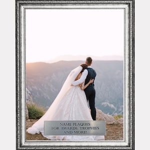 May include: A rectangular silver-toned picture frame with an ornate, textured border. Inside the frame is a photograph of a couple in wedding attire standing on a mountain. A silver plaque at the bottom reads: NAME PLAQUES FOR AWARDS, TROPHIES AND MORE!