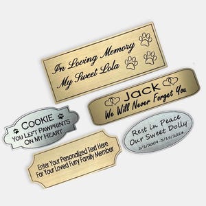 May include: Five gold and silver metal memorial plaques with engraved text. The plaques feature paw prints, hearts, and dates. The text includes "In Loving Memory", "My Sweet Lola", "Jack", "We Will Never Forget You", "Cookie", "You Left Pawprints On My Heart", "Rest in Peace", "Our Sweet Dolly", "2/2/2009-3/15/2024", and "Enter Your Personalized Text Here For Your Loved Furry Family Member".