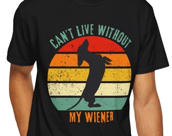 Puede incluir: Camiseta negra con una silueta de perro salchicha frente a un diseño retro de puesta de sol. El texto "CAN'T LIVE WITHOUT MY WIENER" está impreso encima y debajo de la ilustración del perro. Una camiseta divertida e informal.