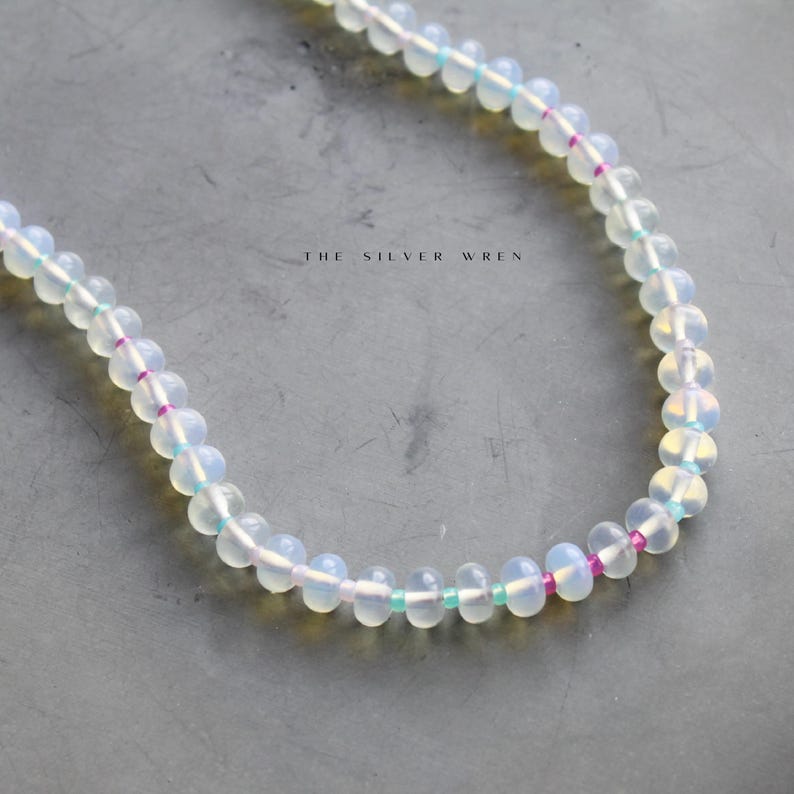 May include: A white opal beaded necklace with pink and turquoise accents. The necklace is made of round beads and is strung on a silver chain.