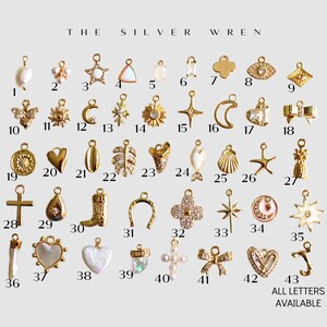 K&ouml;nnte beinhalten: Eine Sammlung von 43 goldfarbenen Charms, darunter eine Vielzahl von Formen wie Sterne, Herzen, Monde, Muscheln und Kreuze. Die Charms sind in Reihen auf wei&szlig;em Hintergrund angeordnet. Der Text "THE SILVER WREN" befindet sich oben im Bild. Der Text "ALL LETTERS AVAILABLE" befindet sich unten im Bild.