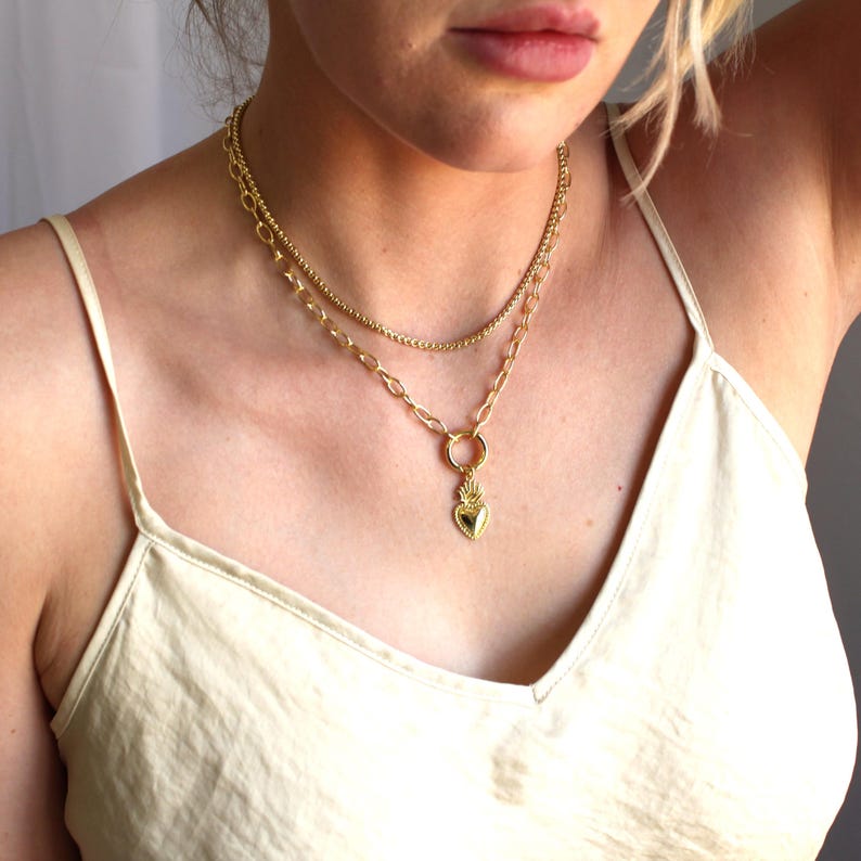 May include: A gold chain necklace with a heart pendant. The heart has a raised design and is attached to a larger ring.