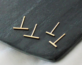 May include: Four gold bar stud earrings on a black surface.