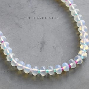 May include: A white opal beaded bracelet with pink and turquoise accents. The bracelet is made with small, round beads and has a delicate, feminine look.