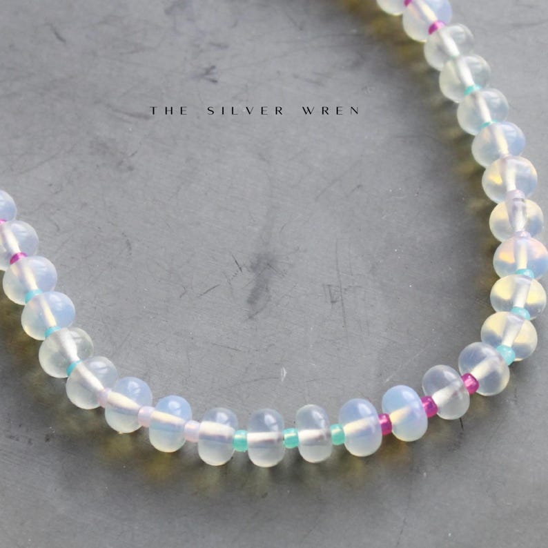 May include: A white opal beaded bracelet with pink and turquoise accents. The bracelet is made with small, round beads and has a delicate, feminine look.