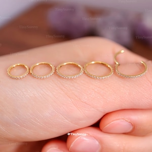 May include: Five gold-colored hoop earrings of varying sizes, each encrusted with small, clear gemstones. The earrings are displayed on a light skin tone background. The brand name "TinySunny" is visible in the image.
