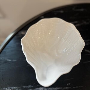 May include: A white, shell-shaped ceramic bowl with a textured surface. The bowl has a scalloped edge and a smooth, glossy finish. The bowl is likely used for serving or display.