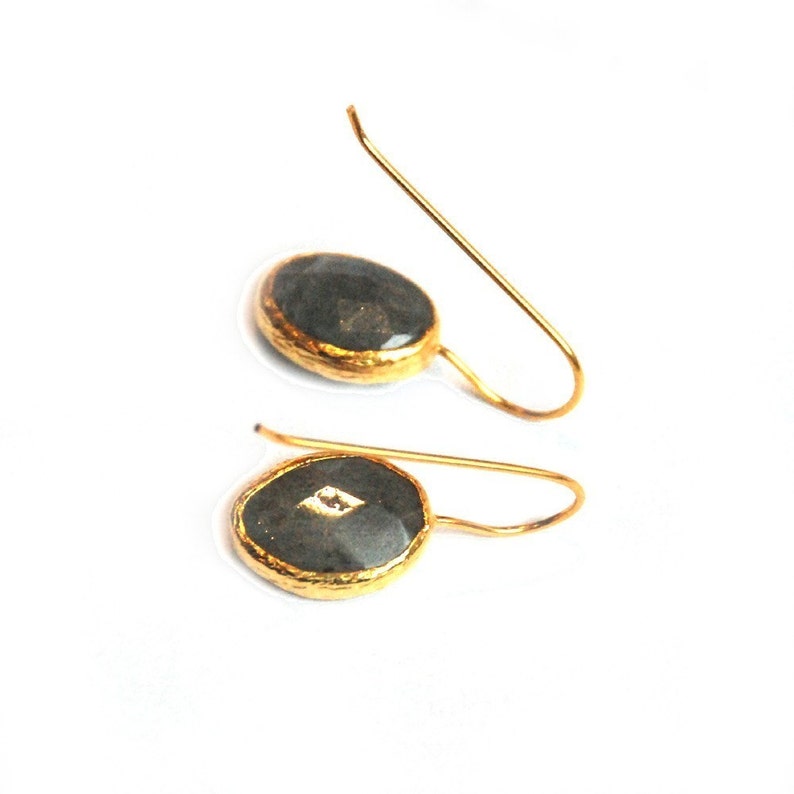May include: A pair of gold earrings with black oval-shaped stones. The stones have a gold rim and a small diamond-shaped stone in the center.