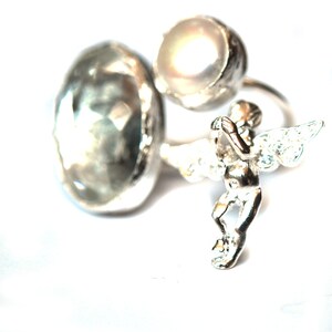 May include: A silver ring with a large faceted gemstone and a small angel charm with wings and a pearl.