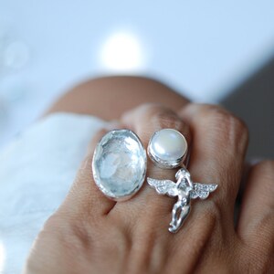 May include: A silver ring with a clear crystal stone, a white pearl, and a silver angel charm.