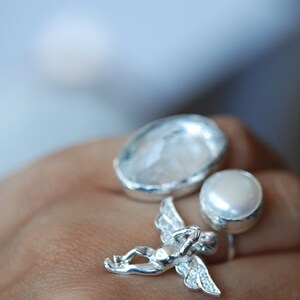 May include: Three silver rings with white stones. The rings feature a round pearl, a large oval stone, and a cherub design.