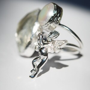 May include: A silver ring with a pearl and a small cherub figurine. The cherub has a wing with small clear stones.