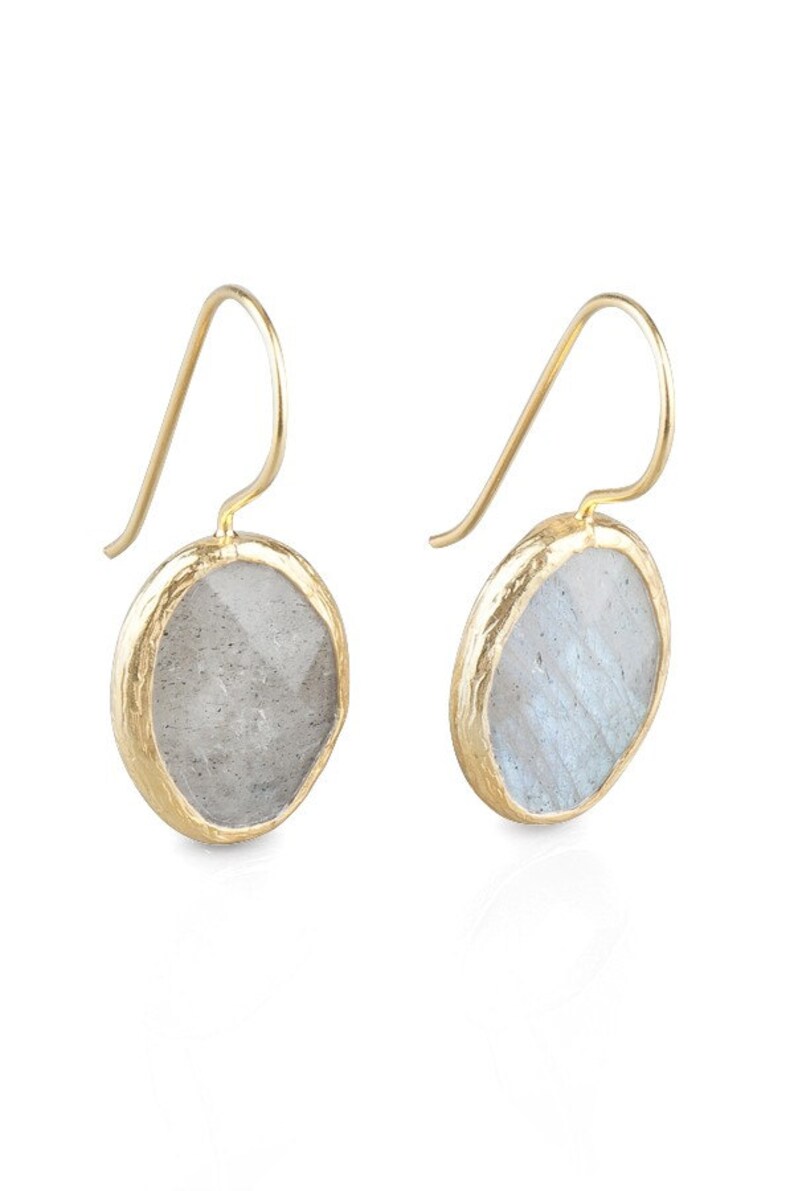 May include: A pair of gold earrings with a round, light gray gemstone set in a gold frame. The earrings have a simple, elegant design.