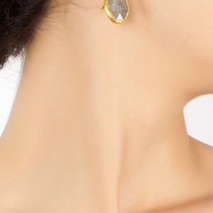 May include: A pair of gold earrings with a gray gemstone. The earrings are drop earrings with a simple design.