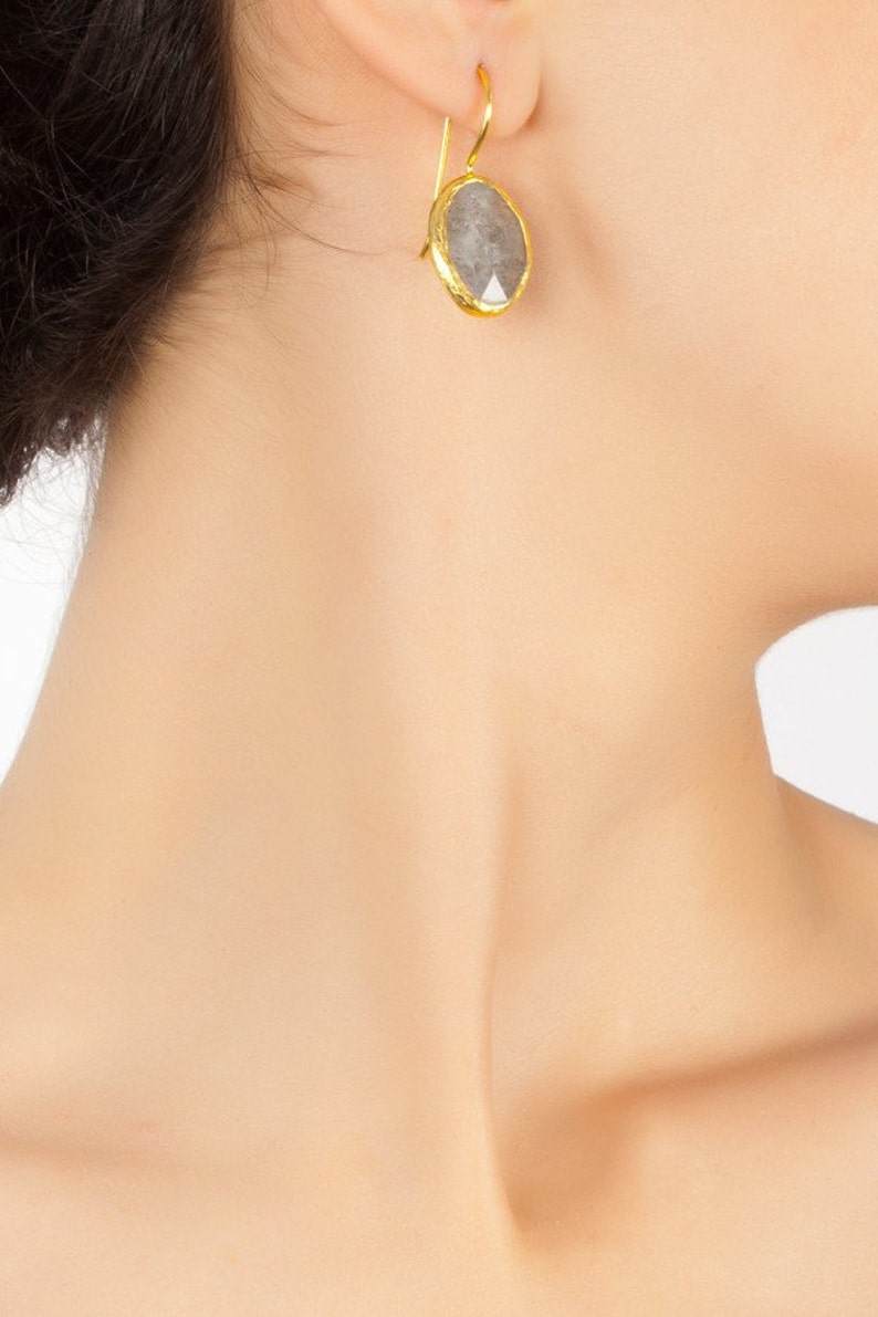 May include: A pair of gold earrings with a gray gemstone. The earrings are drop earrings with a simple design.