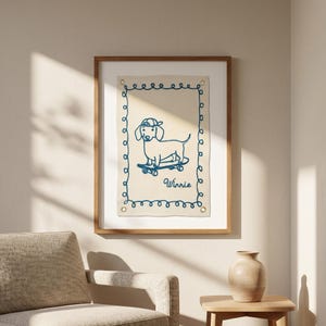 May include: A framed artwork featuring a blue line drawing of a dachshund wearing a cap and riding a skateboard. The artwork is on a beige background with a blue border and the name "Winnie" below the dog.