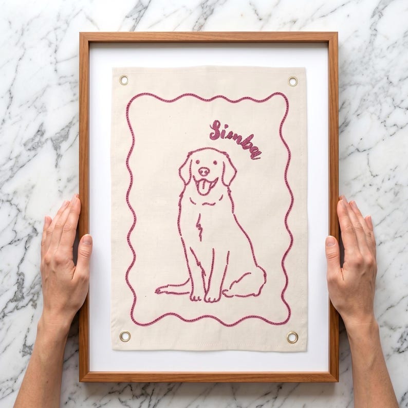 以下が含まれることがあります： 犬のイラストと「Simba」の名前が赤紫で刺繍された、額装されたキャンバスアート。犬とボーダーは同じ色です。フレームは木製です。