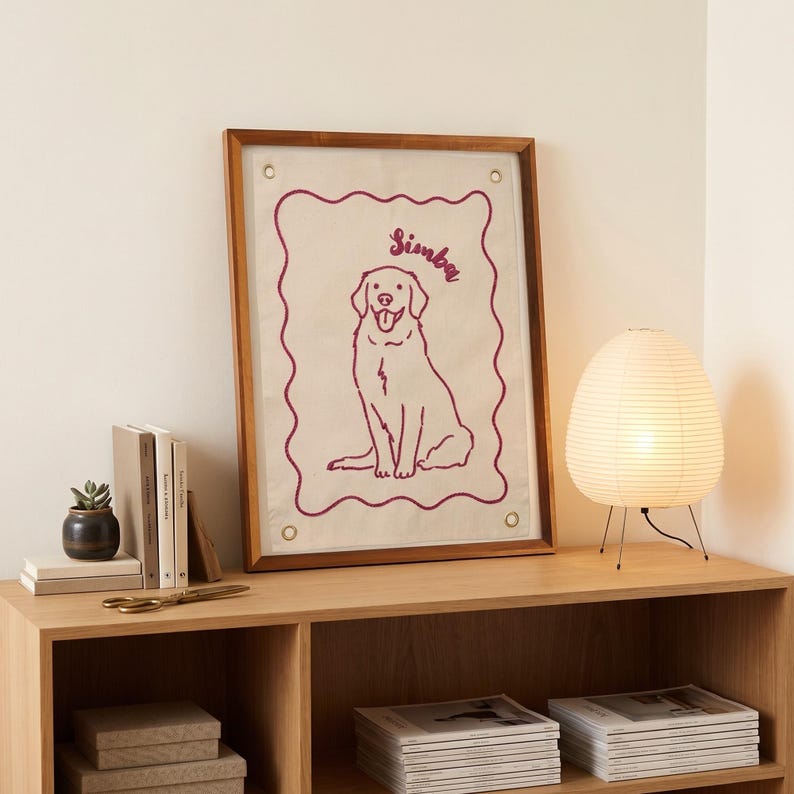 以下が含まれることがあります： 「Simba」という名前が筆記体で書かれた犬の線画が描かれた額入りのアートワーク。 アートワークは木製のフレームに入っており、紙のランタンランプが付いた木製の棚に飾られています。