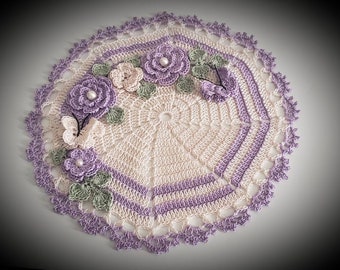 May include: A crocheted doily with a delicate floral design. The doily is made in shades of cream, purple, and green. It features a central circle with a repeating pattern of flowers and leaves.