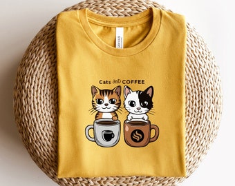 Può includere: Una maglietta gialla con un'immagine di due gatti dei cartoni animati che bevono caffè. Il testo "Cats and Coffee" è stampato sulla maglietta.