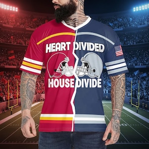 May include: A split-design t-shirt featuring a football theme. One side is red with yellow stripes and a helmet graphic, the other is navy blue with a gray helmet graphic and an American flag. The text "HEART DIVIDED HOUSE DIVIDE" is printed on the shirt.